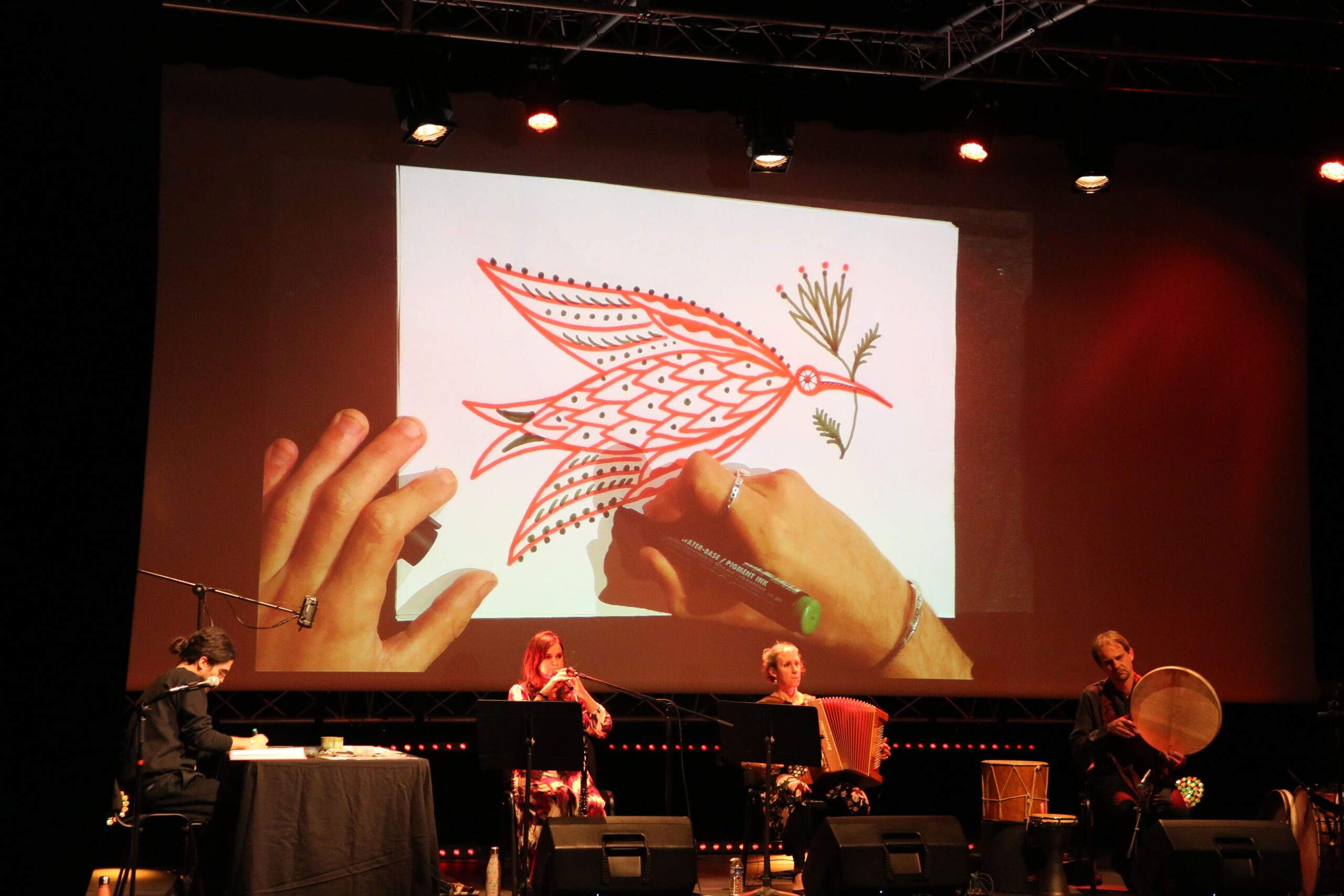 3 musiciens sont sur scène avec un dessinateur qui illustre les chansons qu'ils jouent